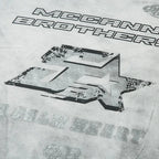 Gray t-shirt with 'McCann Brothers' and 'Adalbert' text and graphics on a textured background