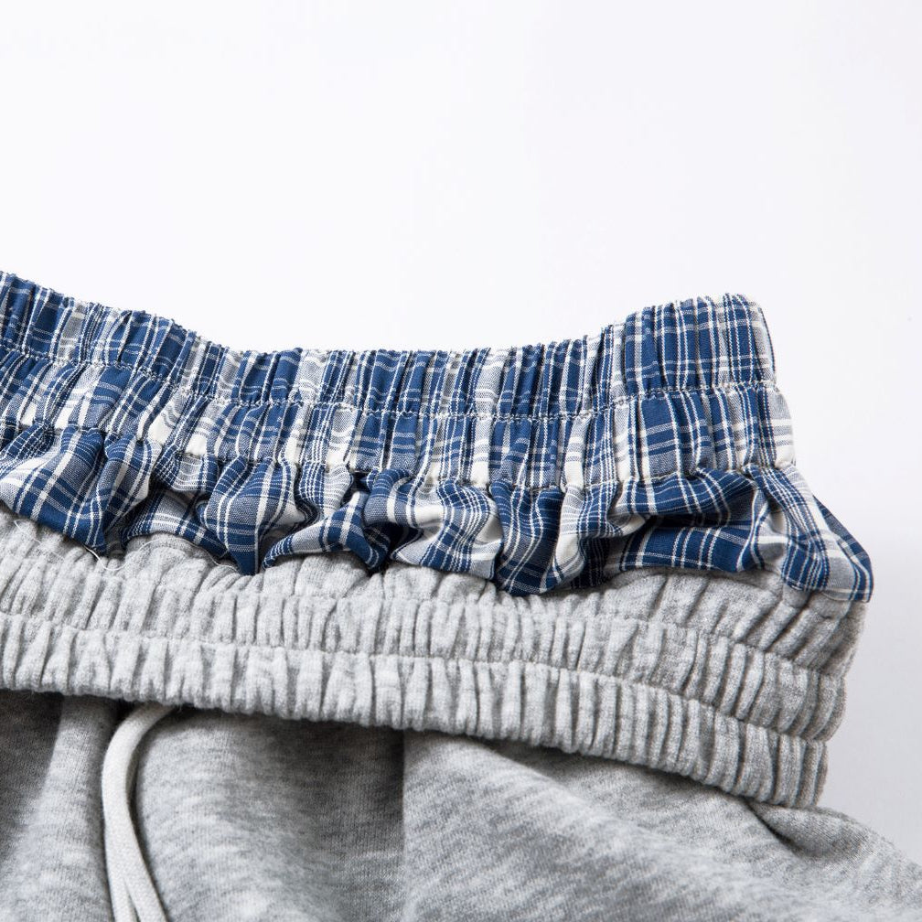 Stack of folded clothes including a plaid shirt and gray pants on a white background
