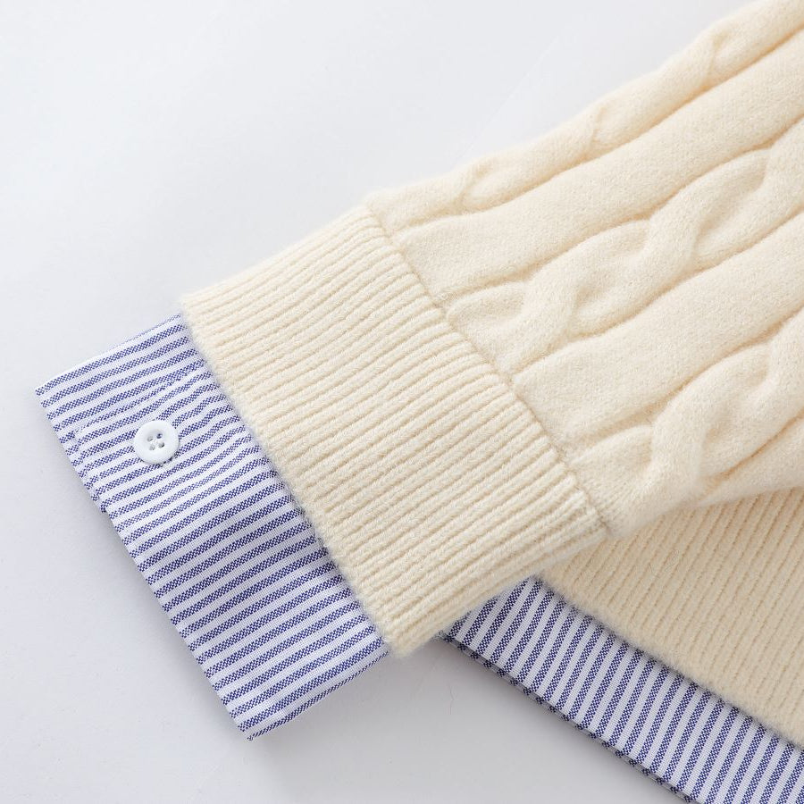 Close-up of a cream-colored cable-knit sweater with blue striped cuffs on a light gray background