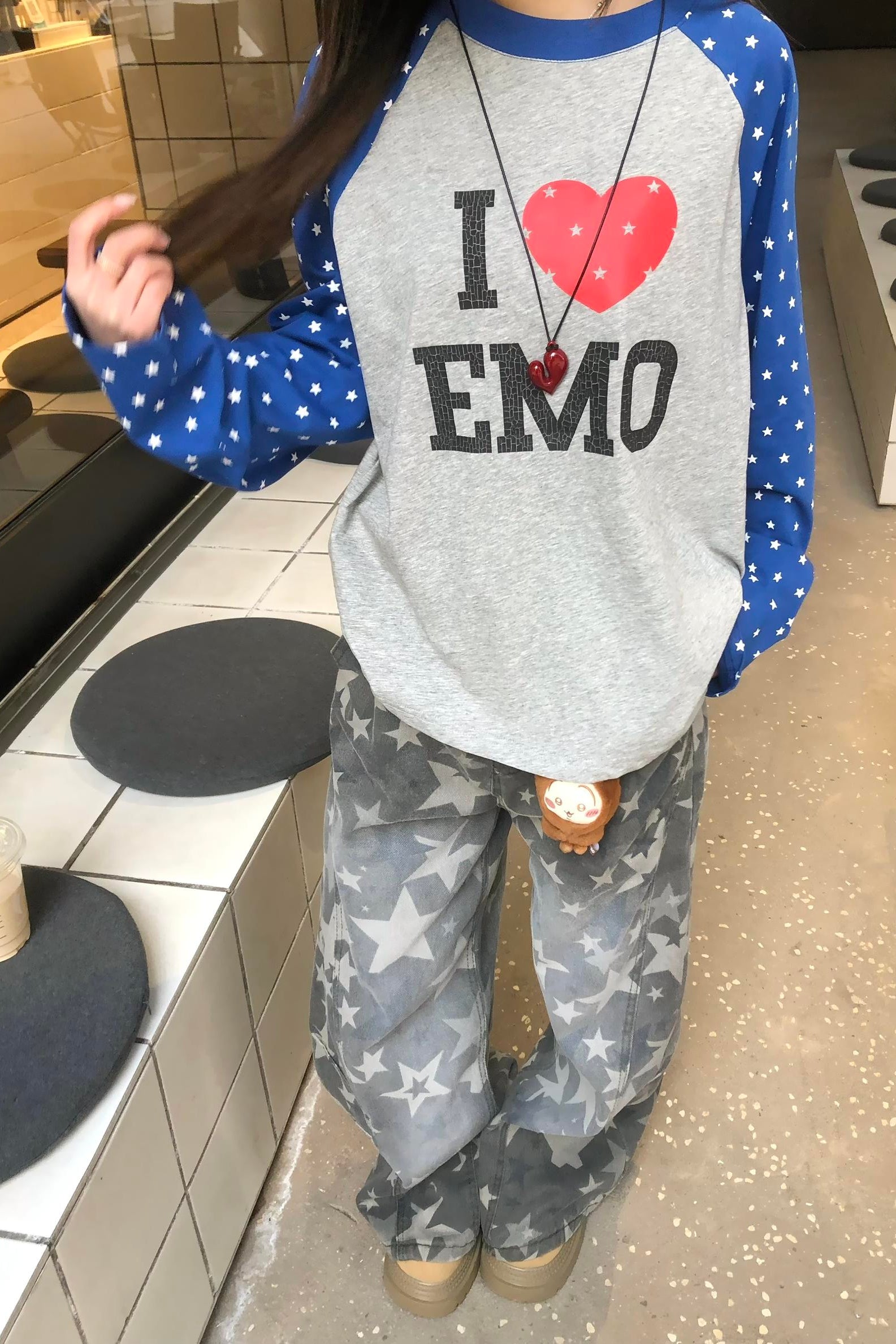 Person wearing a gray sweatshirt with 'I ❤️ emo' text and star-patterned pants in an indoor setting.