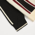 Close-up of a black, beige, and red striped sweater sleeve on a light gray background